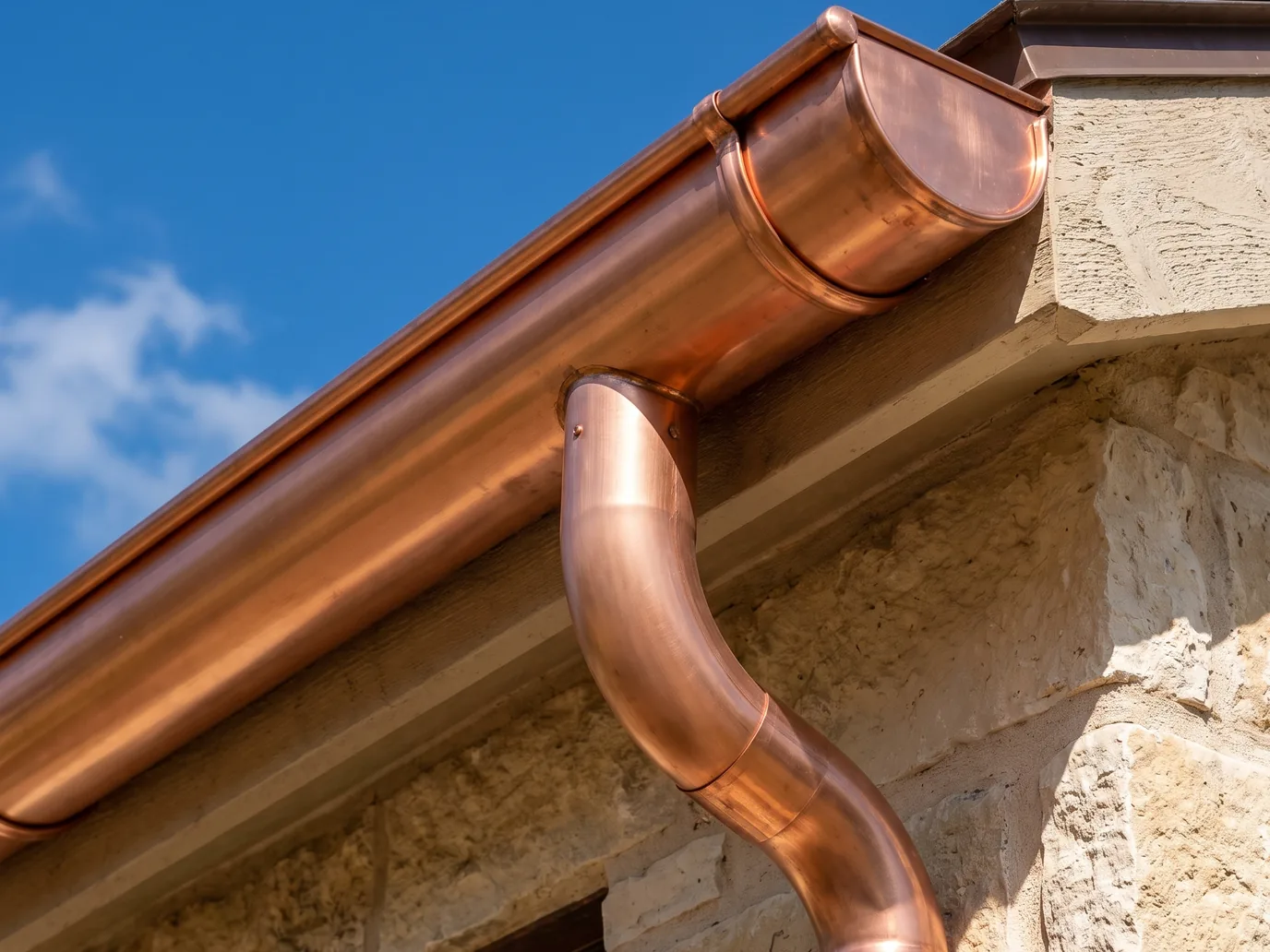 A new copper half-round gutter with an end cap, a round outlet, and a round copper downspout on a limestone eave